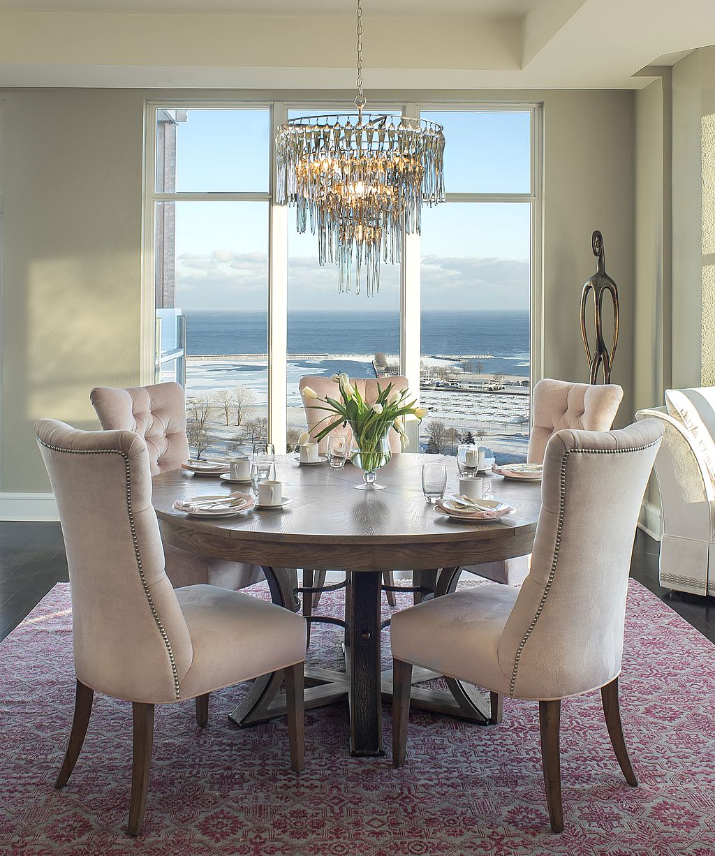 A transitional dining room overlooking water uses a soft pink velvet fabric juxtaposed with a brighter pink rug.